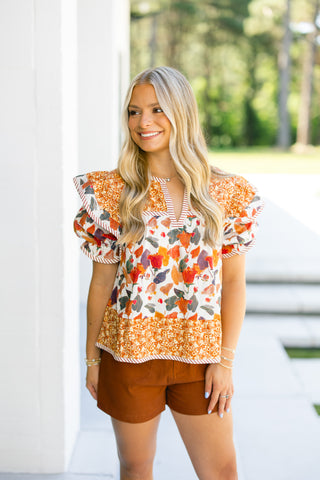 Woman wearing a colorful floral blouse and brown shorts outdoors.