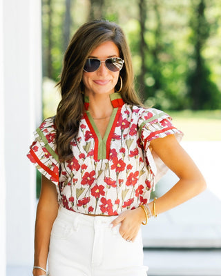 Woman wearing a red floral blouse and white pants, standing outdoors.
