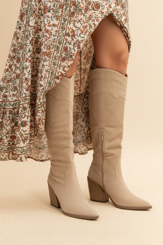 Beige knee-high boots worn with a patterned dress on a neutral background