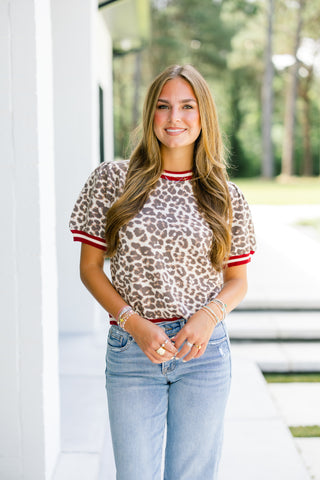 Woman wearing a leopard print top with red trim and light blue jeans outdoors.