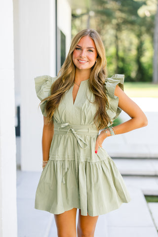 Woman wearing a light green dress with ruffled sleeves outdoors.
