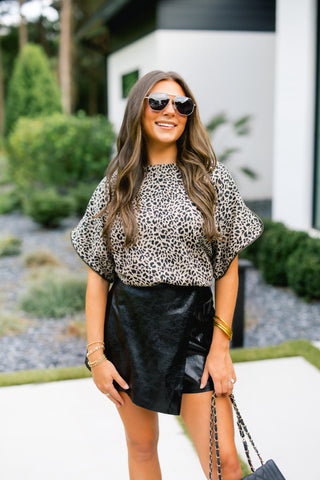 Woman wearing a leopard print top and black leather skirt outdoors.