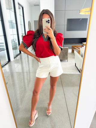 Person taking a mirror selfie wearing a red top featuring green plaid accents.