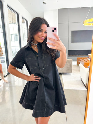 Woman taking a mirror selfie wearing a black dress in a modern living room.