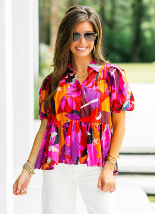 Woman wearing a colorful patterned blouse and white pants outdoors.