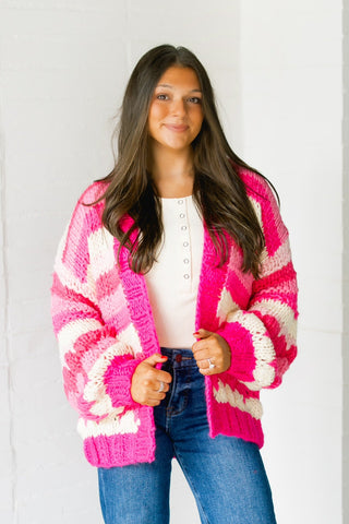 Woman wearing a pink and white patterned cardigan standing in front of a white wall.