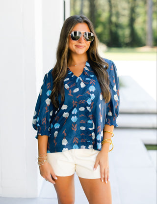 Woman wearing a blue floral blouse and white shorts outdoors.