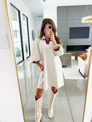 Woman taking a mirror selfie wearing a white dress and knee-high boots in a modern living room.