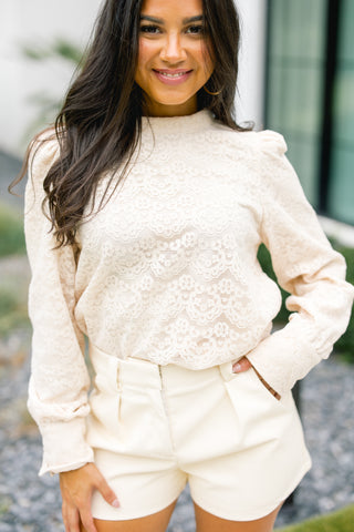 Woman wearing a cream-colored lace top and shorts.