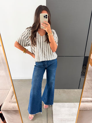 Woman taking a mirror selfie wearing a striped shirt and blue jeans.