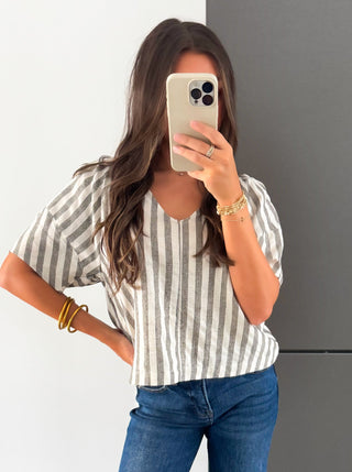 Woman taking a mirror selfie wearing a striped shirt and blue jeans.