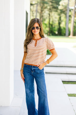 Woman wearing a camel striped short sleeve lightweight sweater and blue jeans outdoor