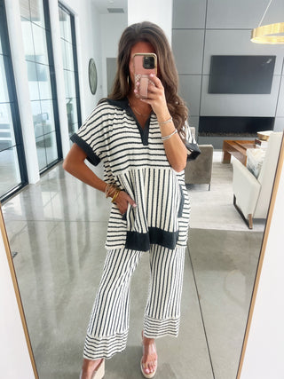 Woman taking a mirror selfie wearing a black and white striped outfit in a modern living room.