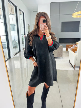 Woman taking a mirror selfie wearing a black dress with red trim in a modern living room.