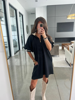 Person wearing a black dress with white trim in a modern living room.