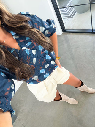 Woman in a blue floral dress sitting on a concrete floor.