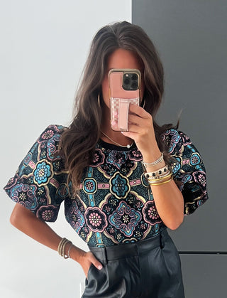 Woman taking a mirror selfie wearing a floral top and black shorts with knee-high boots.